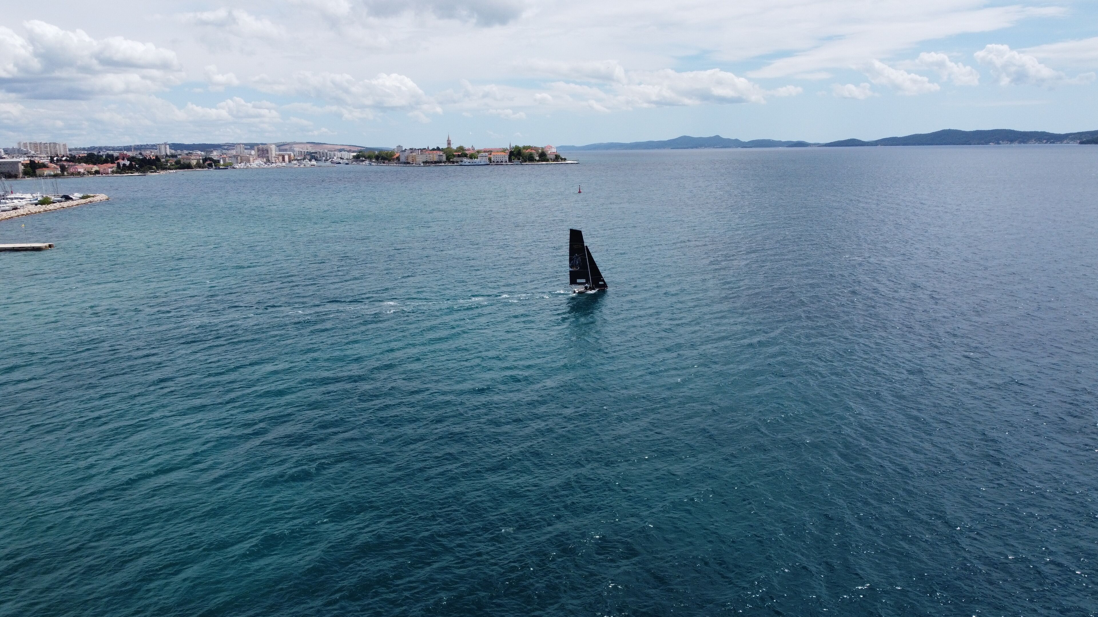 Ein Segelboot auf ruhiger See vor einer entfernten Stadtlandschaft.