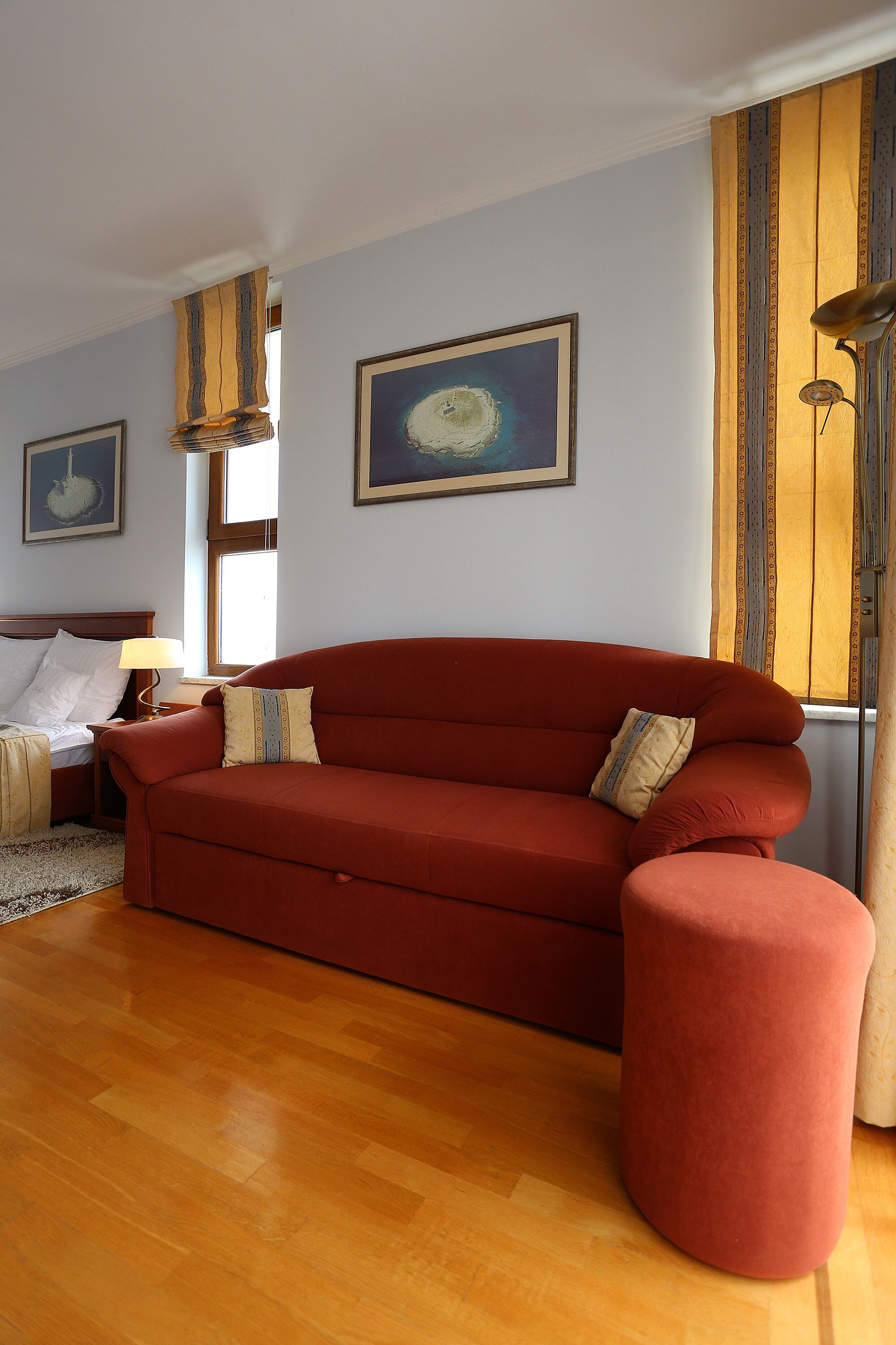 Un salon avec un canapé rouge, un plancher en bois et un lit avec une table de chevet.