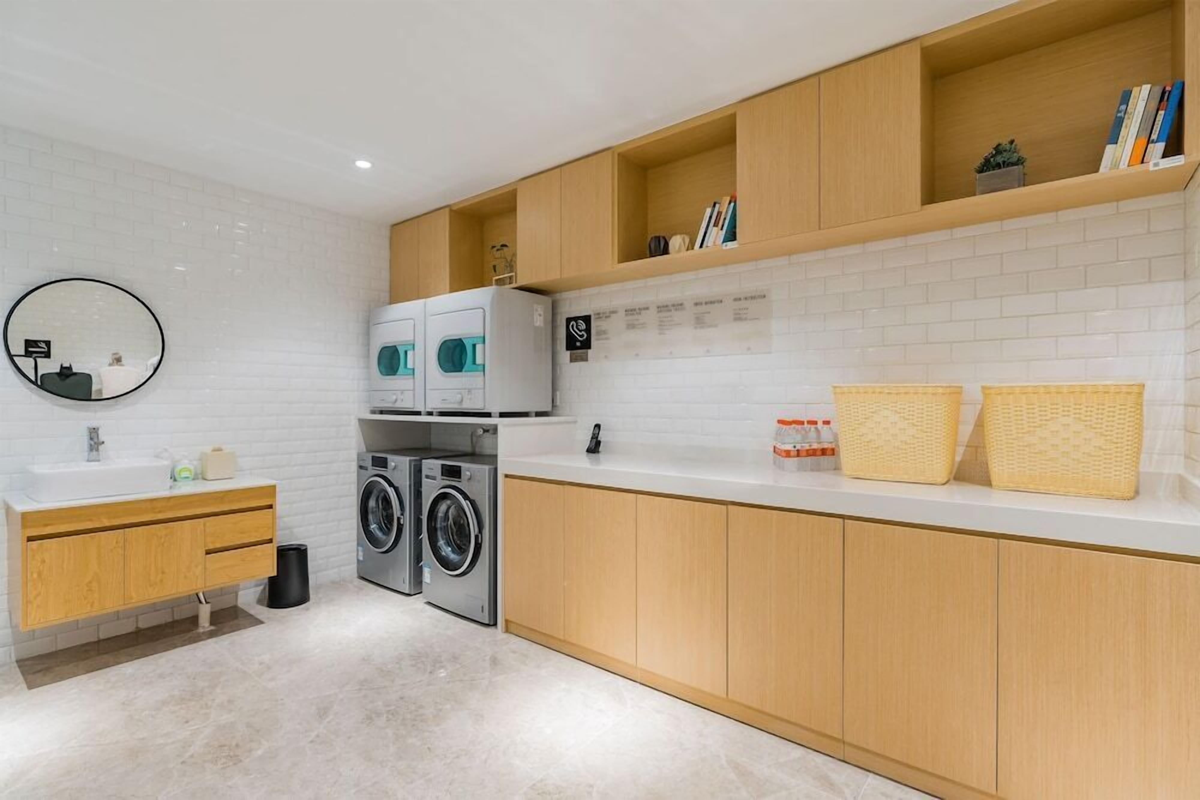 A modern kitchen with white subway tiles, wooden cabinets, a built-in washing machine, and a round mirror.