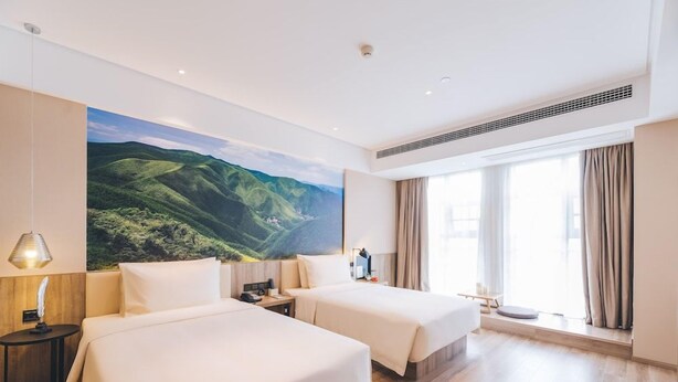 A hotel room with two beds, a large window with curtains, a painting of a landscape, and a small table with a lamp. - Atour Hotel (Xi'an)