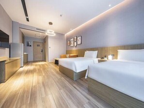 Une chambre d’hôtel avec deux lits, un plancher en bois, une kitchenette et une salle de bain visible à travers une porte ouverte.