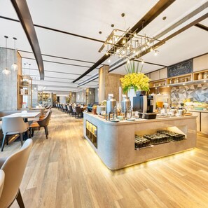 Un café moderne doté d’un bar central, de différents espaces pour s’asseoir et d’un comptoir de cuisine visible.