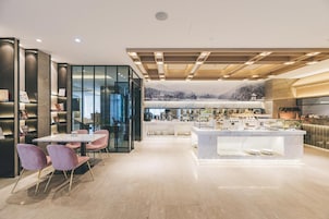 A modern hotel lobby with a dining area, a reception desk, and a view of a mountainous landscape.