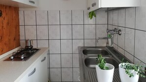 Keittiössä on valkoiset kaapit, kaasuliesi, pesuallas ja seinällä koristeellinen lautanen.