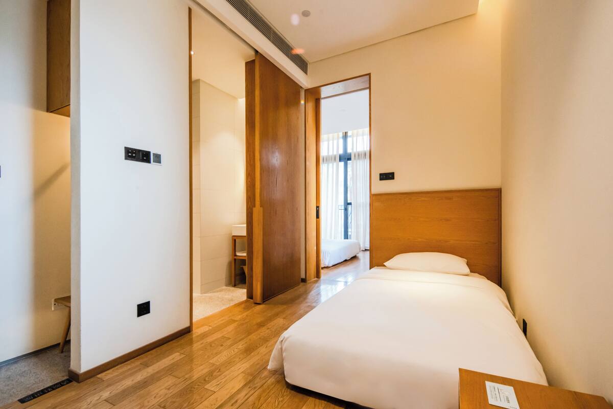 Une chambre d’hôtel avec un plancher en bois, un lit avec une literie blanche, une tête de lit en bois et une porte donnant sur une autre pièce.