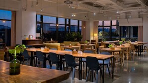 Un vaste espace dédié à la salle à manger, avec de nombreuses tables et chaises, de grandes fenêtres offrant une vue sur le paysage urbain, et un plafond moderne agrément é de luminaires.