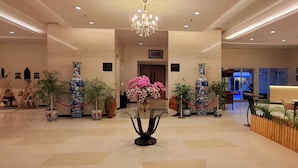 Un hall d’entrée spacieux, agrémenté d’un lustre, de plantes en pot et d’un comptoir de réception.