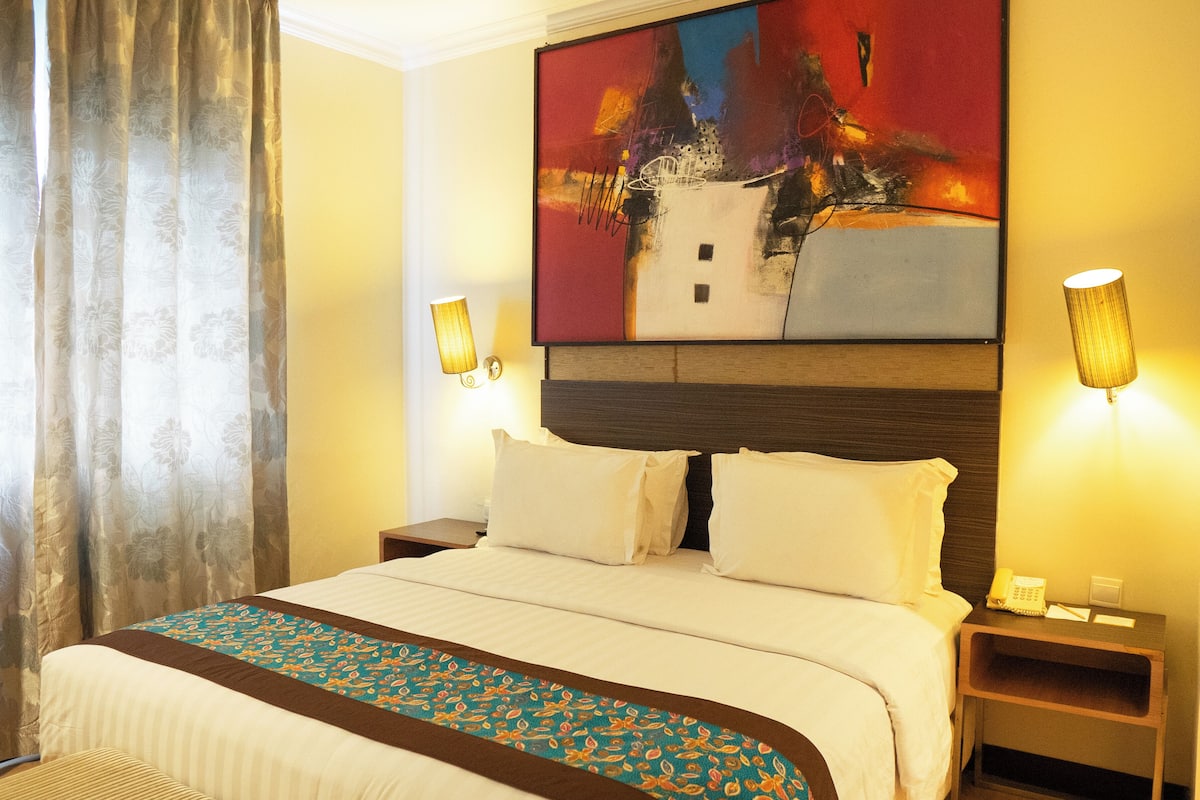 Habitación de hotel con una cama grande, dos mesitas de noche, una lámpara y un cuadro en la pared.