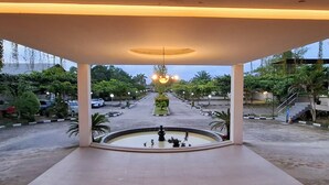 Un espace extérieur abrité doté d’une fontaine centrale, entouré d’une allée pavée et bordé d’arbres et de lampadaires.