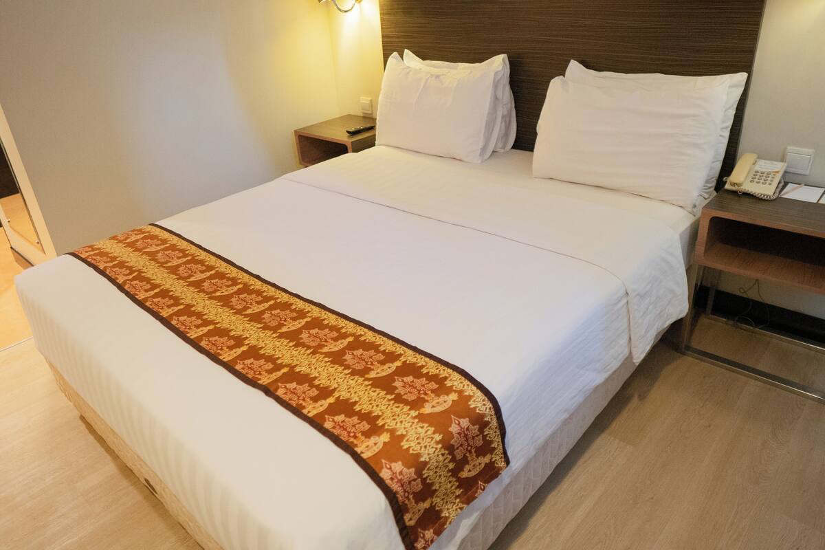 Habitación de hotel con una cama grande, cabecera de madera, mesita de noche con teléfono y mesita de noche con lámpara.