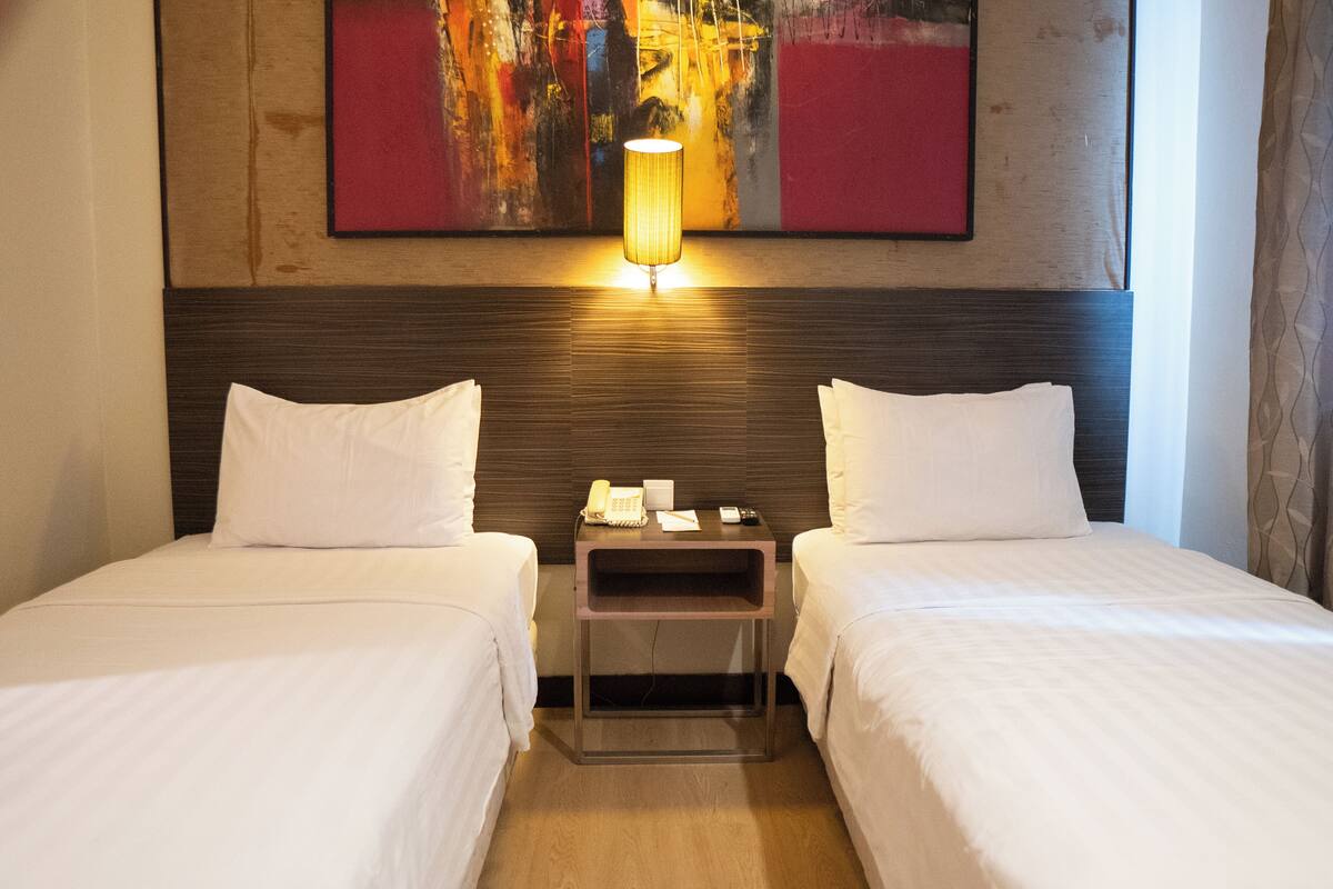 Una habitación de hotel con dos camas, una mesita de noche con lámpara y un cuadro en la pared.
