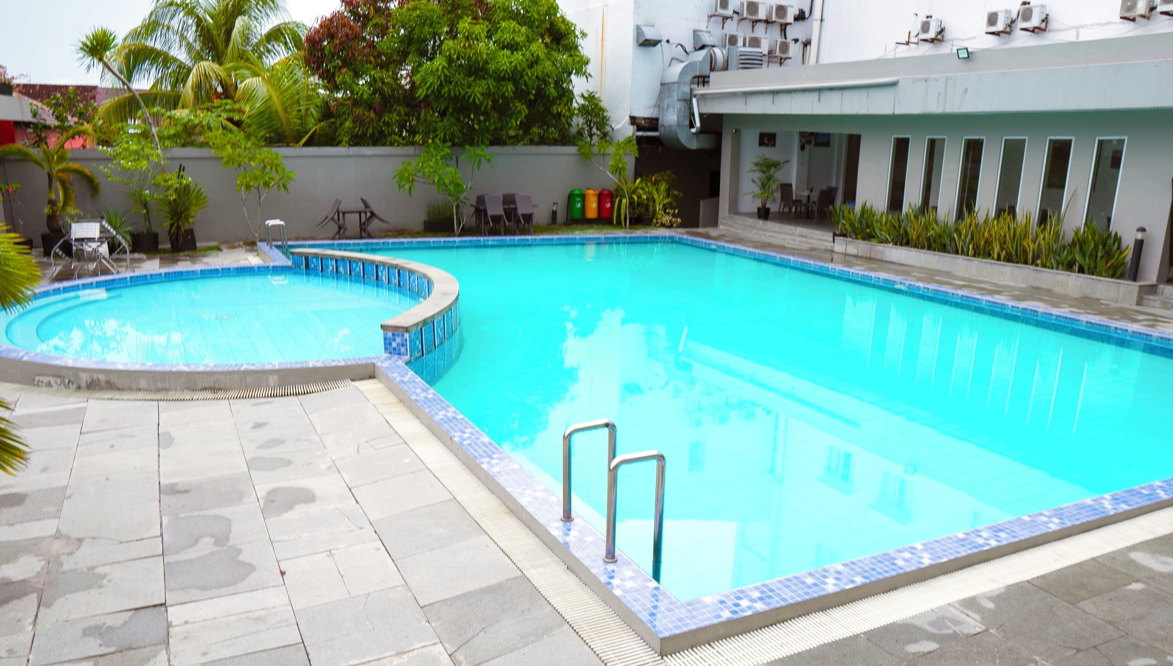 Una piscina con borde de azulejos, una sección circular pequeña y una escalera metálica.