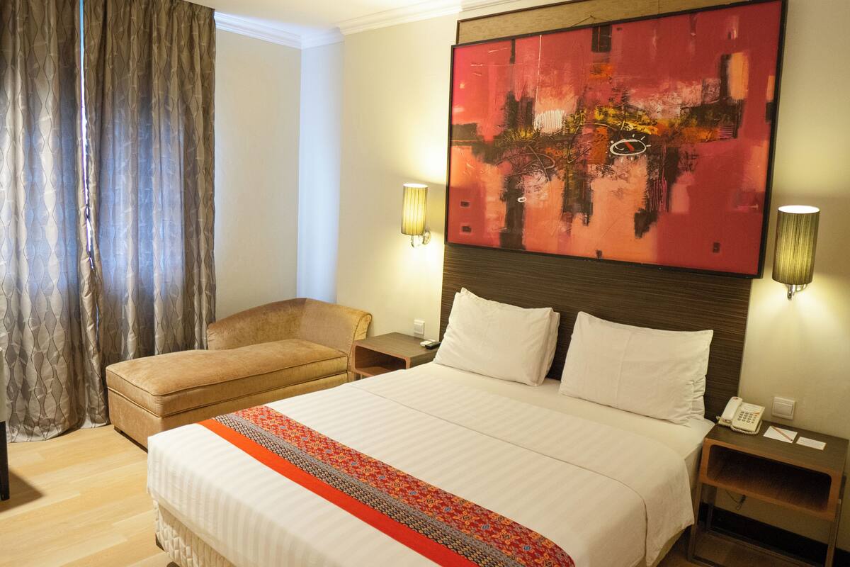 Habitación de hotel con una cama grande, un sofá, dos lámparas de noche, un teléfono y un cuadro en la pared.
