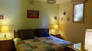 A bedroom with a bed, two bedside lamps, a painting on the wall, and a window with blinds.