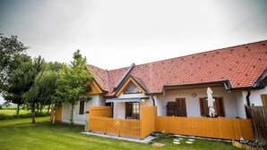A two-story house with a red-tiled roof, a wooden fence, and a well-maintained lawn. - Golf Apartment (Moravske Toplice)