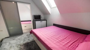 A bedroom with a bed, a wardrobe, a small table with a TV, and a skylight. - Golf Apartment (Moravske Toplice)