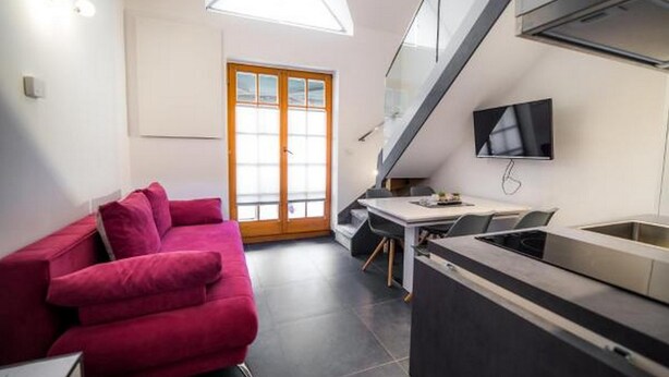 A compact kitchen with a dining area, a red sofa, and a TV mounted on the wall. - Golf Apartment (Moravske Toplice)