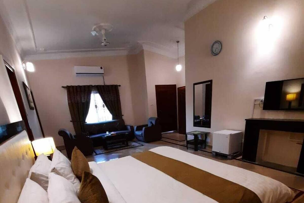Habitación de hotel con una cama grande, un escritorio con lámpara, un televisor y un reloj en la pared.