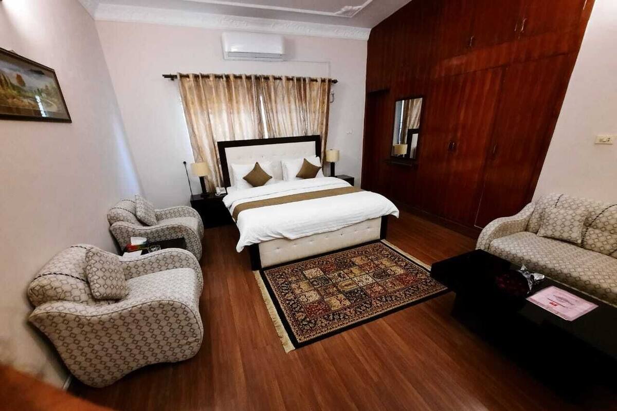 Una habitación de hotel con una cama grande, dos sillones, un sofá y una alfombra estampada.