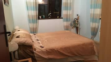 A bedroom with a bed, a window with curtains, a bedside table with a lamp, and a small plant.