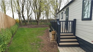 Il s’agit d’une propriété résidentielle avec un chemin pavé menant à la porte d’entrée, un petit jardin avec de la pelouse et une clôture en bois, et un arrière-plan bordé d’arbres.