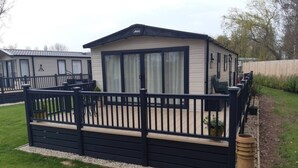 Une maison mobile dotée d’une terrasse clôturée, de grandes fenêtres et d’un petit jardin.