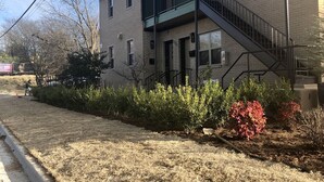A two-story building with a brick exterior, a metal staircase, and a small garden area with shrubs and a tree. - Great Monthly Furnished Apartment in Downtown LR (Little Rock)
