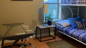 A bedroom with a bunk bed, a desk with a chair, a small table with a lamp, a framed picture on the wall, and a window with a view of the outdoors. - Great Monthly Furnished Apartment in Downtown LR (Little Rock)