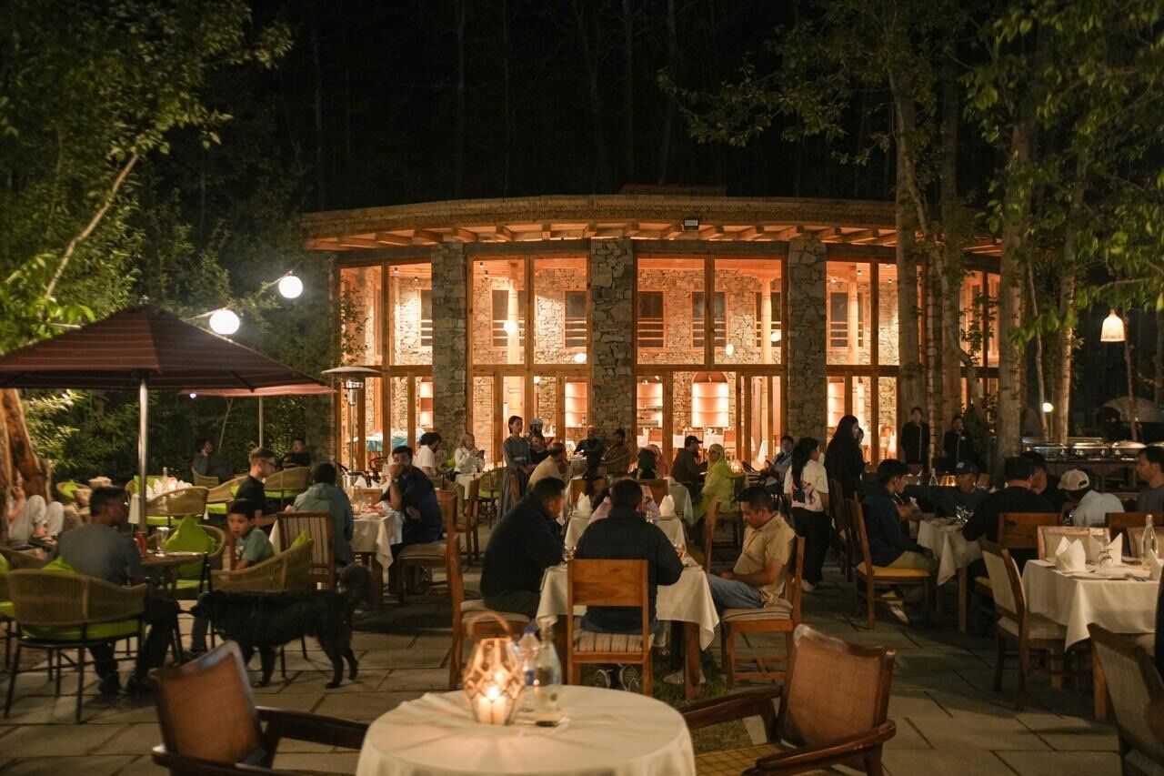 An outdoor dining area with stone walls and tables, surrounded by trees.