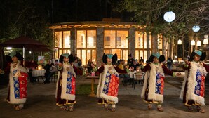 Un grupo de personas bailando una danza tradicional frente a un edificio con amplias ventanas y fachada de piedra.