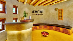 Un área de recepción con un mostrador de madera, un cartel en la pared que dice "AMCHI SPA" y un banco con un cuenco decorativo.