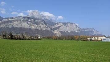 Un paysage montagneux avec un champ verdoyant au premier plan et un bâtiment avec un toit rouge en arrière-plan.