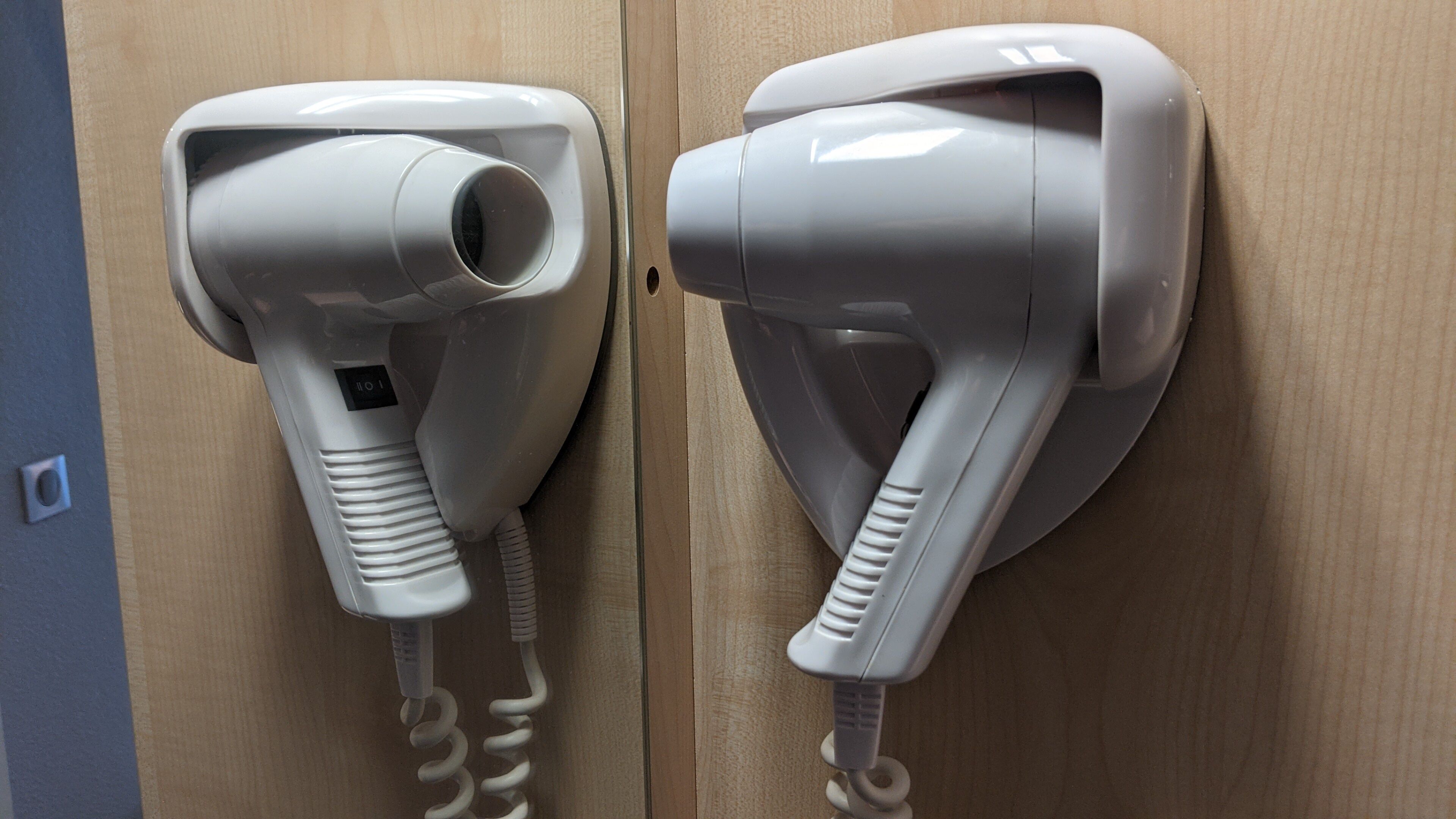 Two hair dryers mounted on a wooden wall, each with a power cord.