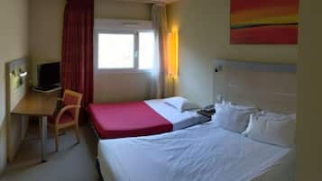 A hotel room with a bed, a desk, a chair, a TV, and a window with curtains.