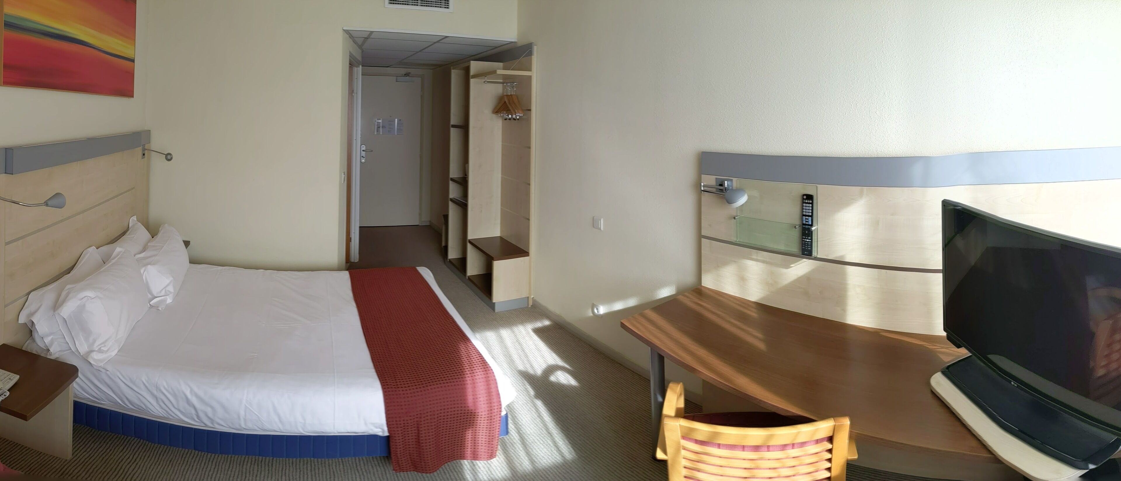 Une chambre d’hôtel avec un lit, un bureau avec une télévision, une chaise et une porte de salle de bain.