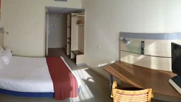 A hotel room with a bed, a desk with a TV, a chair, and a bathroom door.