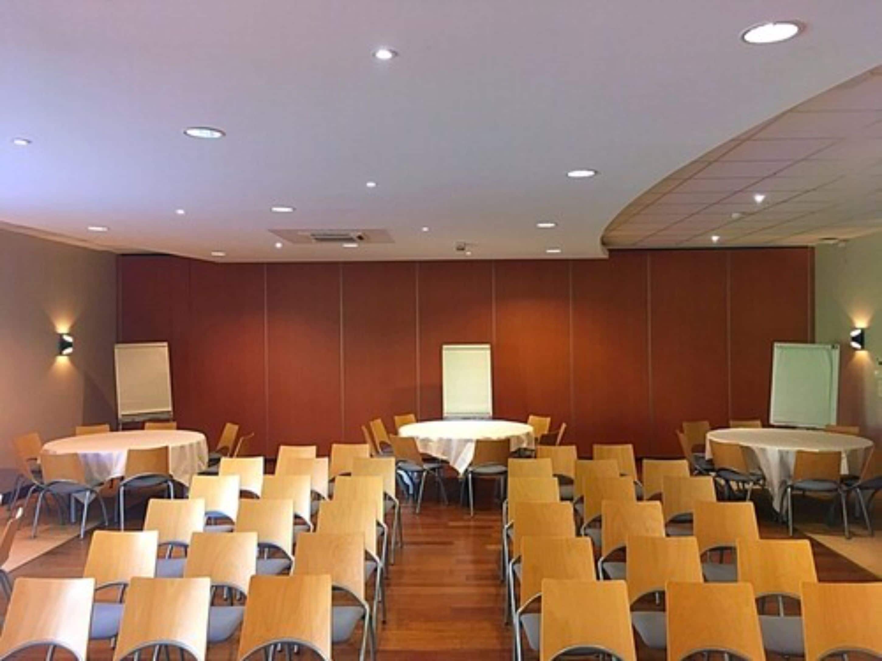 Una sala de conferencias con varias mesas y sillas, equipada con pizarras y iluminación colgante.