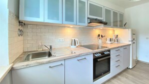 A modern kitchen with white cabinets, a stainless steel sink, a built-in oven, and a coffee maker. - Experience Chiemsee, mountains & lakes - apartment for up to 4 people, 2 bedrooms, balcony (Marquartstein)