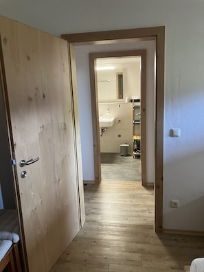 Ein Flur, der zu einem Badezimmer mit Waschbecken, Spiegel und Toilette führt.