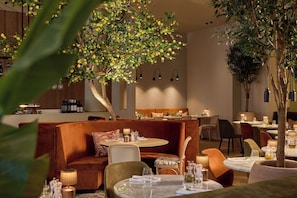 A restaurant with a cozy seating area, a bar, and a large tree. - Van der Valk Hotel Gent (Ghent)