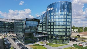 A modern hotel with a curved glass facade, a parking lot, and a landscaped area with benches.