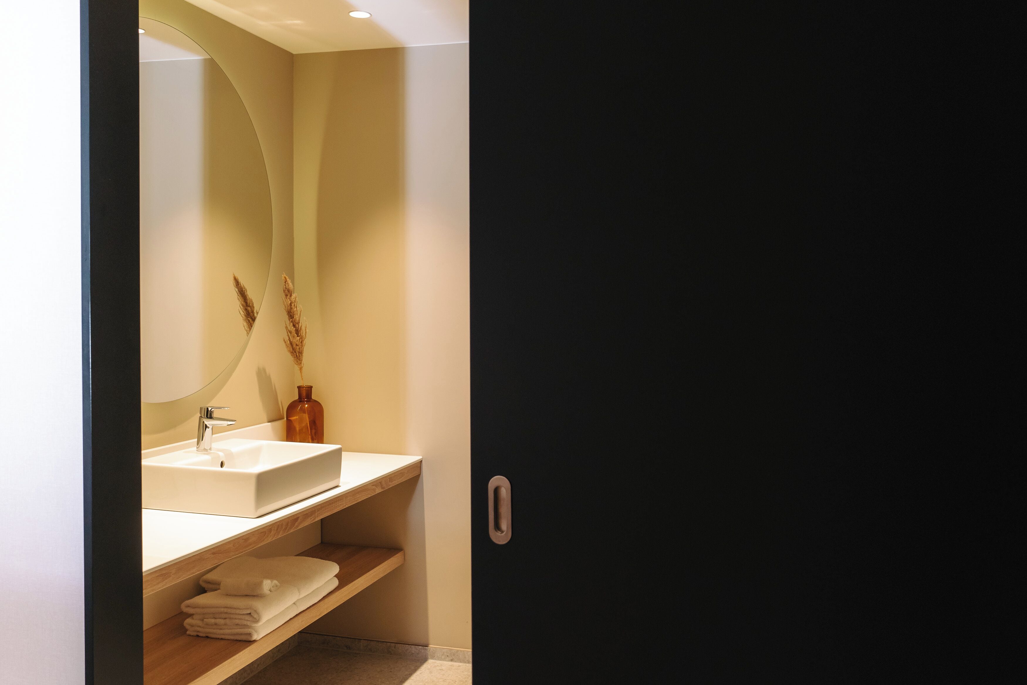 A modern bathroom with a white sink, mirror, and wooden shelves.