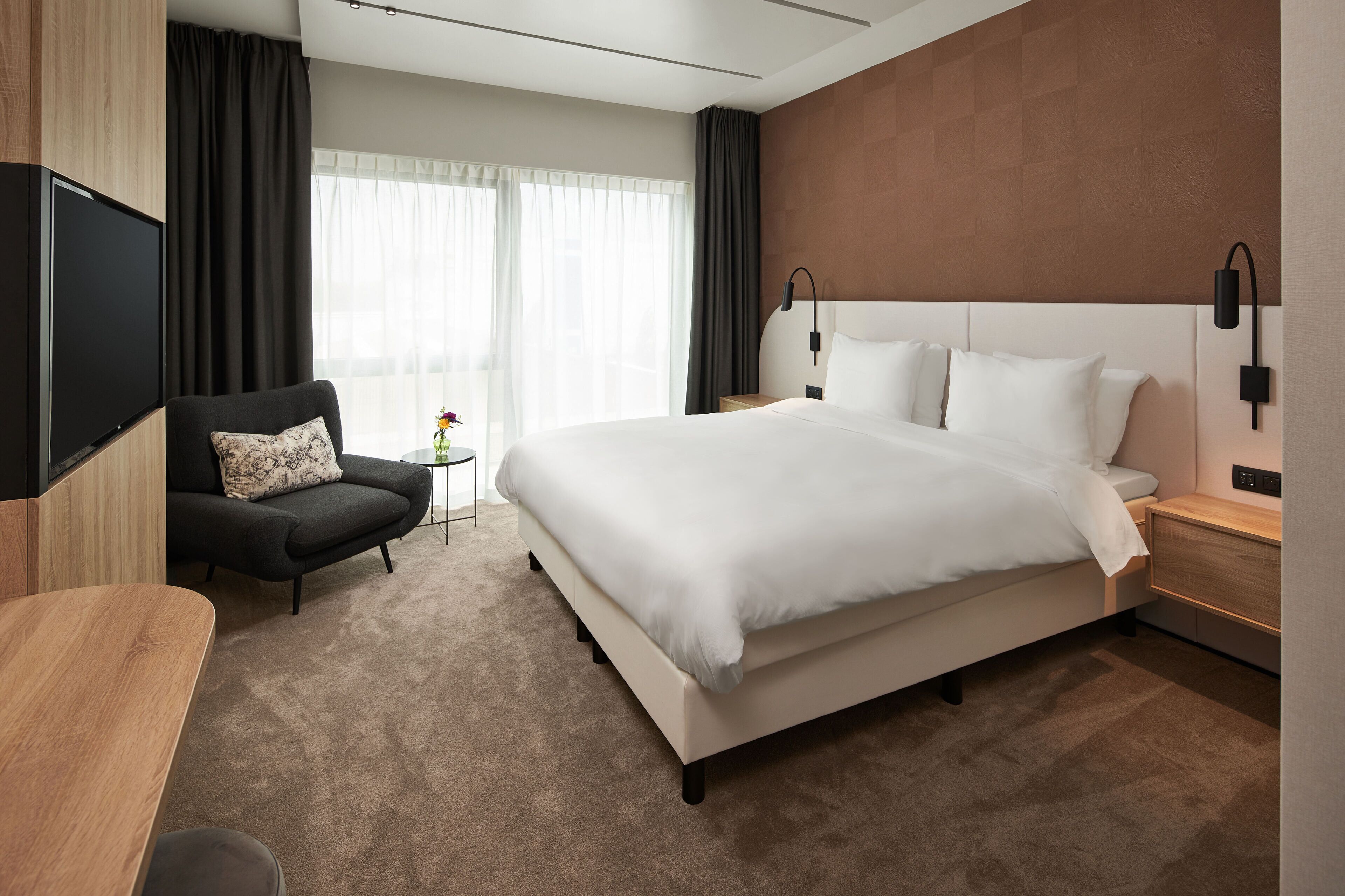 A modern hotel room with a large bed, a flat-screen TV, a sofa, and a small side table.