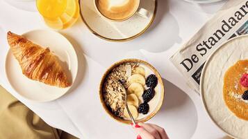 Desayuno con croissant, fruta y café sobre una mesa.