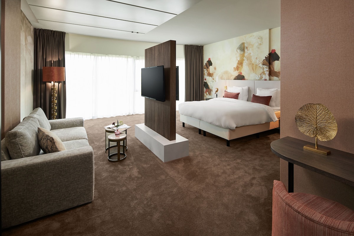 A modern hotel room with a large bed, a sofa, a TV, and a small table.