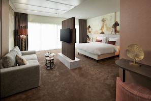 Una habitación de hotel moderna con una cama grande, un sofá, un televisor y una mesita.
