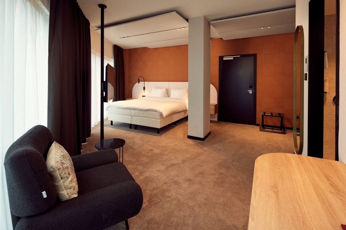 A modern hotel room with a large bed, a sofa, a small table, and a door.