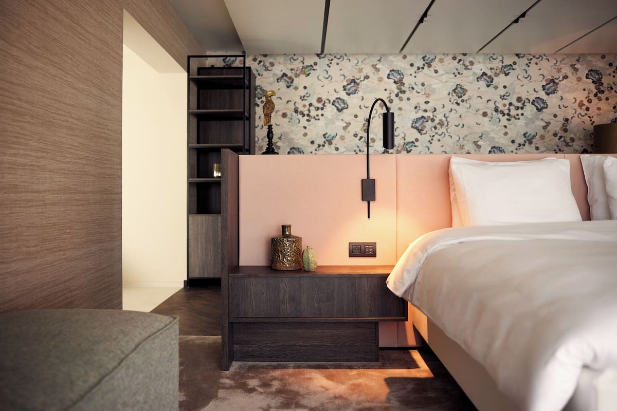 A modern bedroom with a bed, a nightstand, a lamp, and a decorative wall.