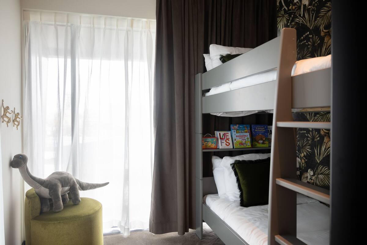 A child's bunk bed with a dinosaur toy, a small stool, and children's books on the shelf.