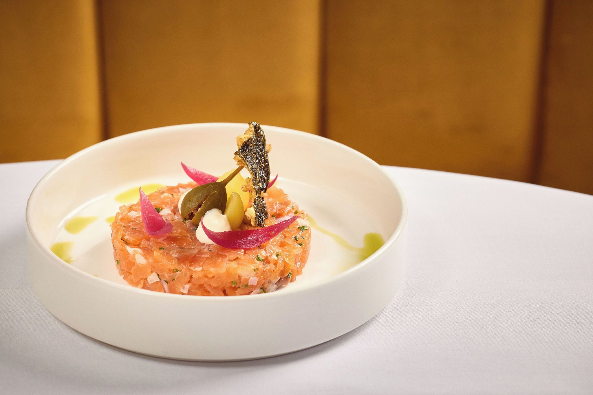 Un plato blanco con una porción de tartar de salmón, adornado con pescado, cebolla roja y hierbas.